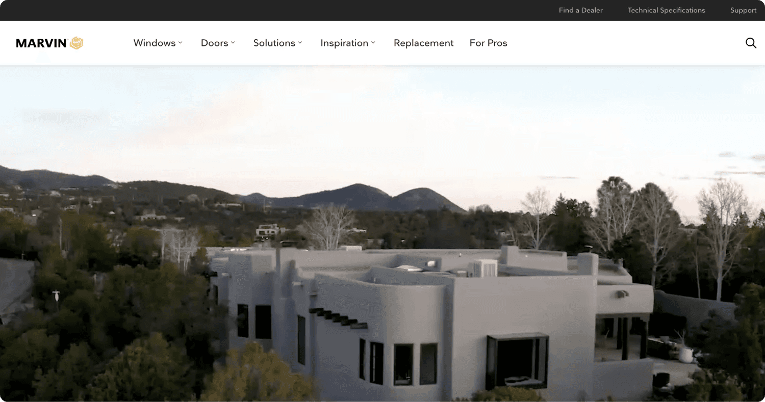 marvin homepage Aerial view of a modern house surrounded by trees, with mountains in the background under a clear sky.